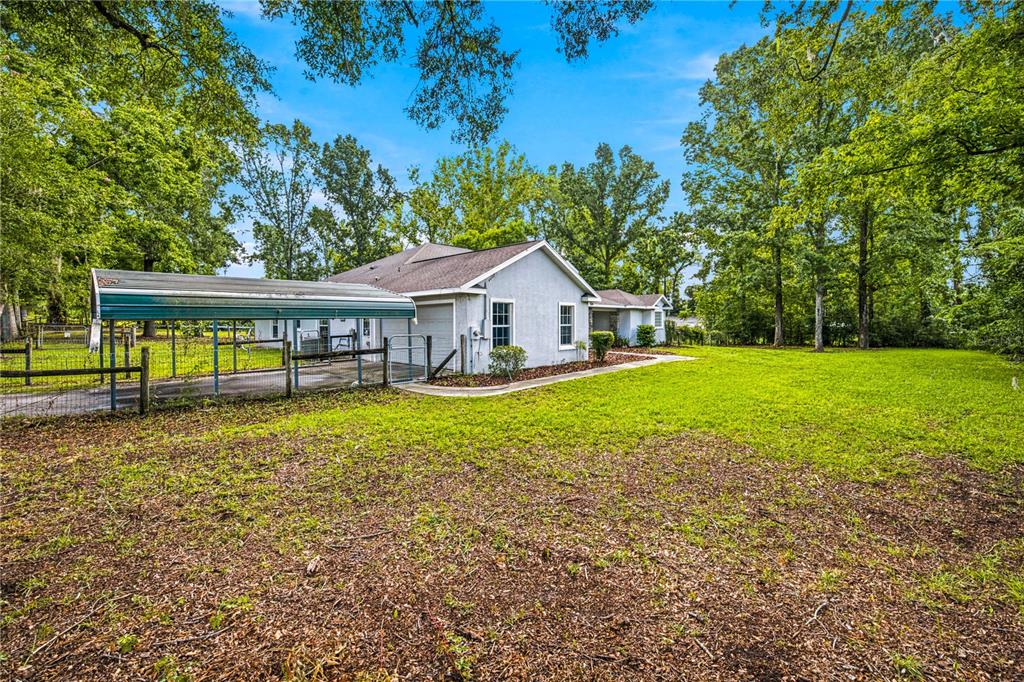 A single-story house with a metal carport sits on a large, grassy, tree-lined lot — 5259 SE 38TH STREET, OCALA, FL