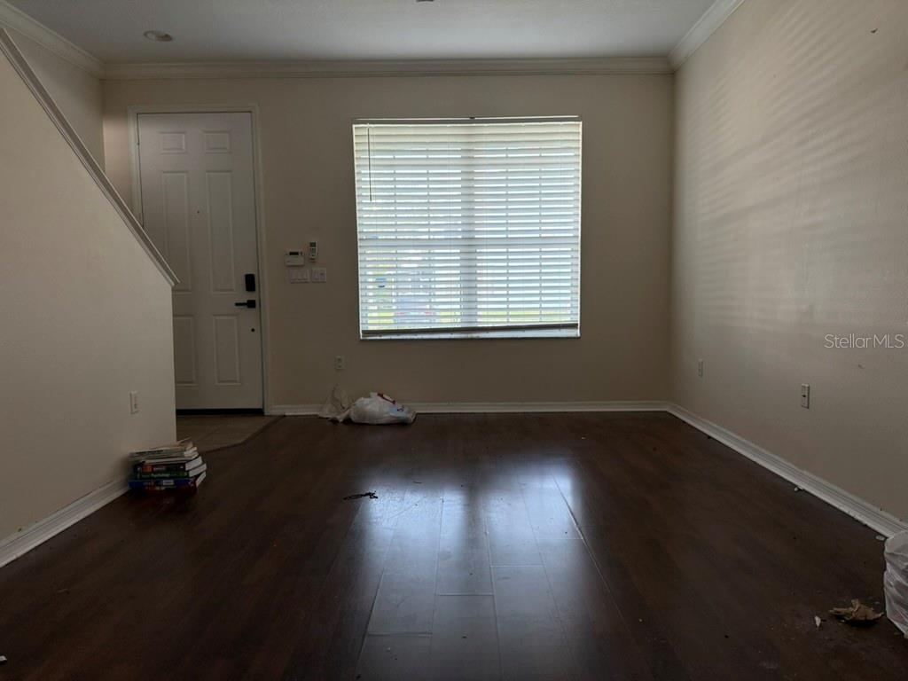 An empty room with dark wood-look flooring, beige walls, and a single window with blinds — 11537 DECLARATION DRIVE, TAMPA, FL