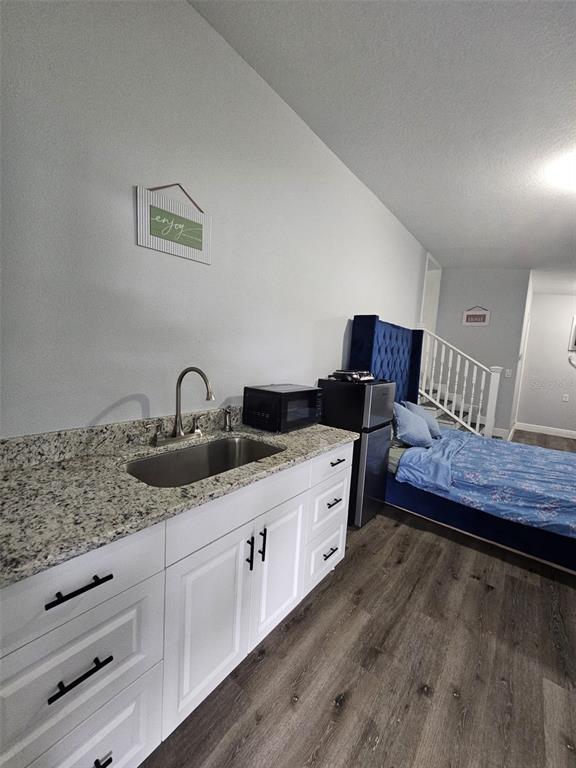 A kitchenette with granite countertops and white cabinets sits beside a bed in a room — 6928 SALINAS DRIVE, ORLANDO, FL