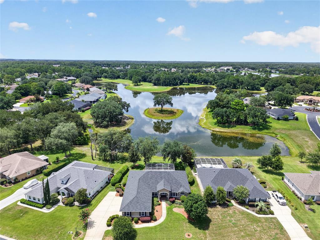 An aerial view shows three suburban houses situated along a lake with a small island — 349 LAKE DRIVE, OCALA, FL