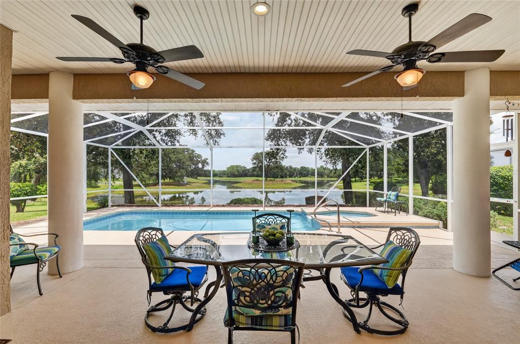 A covered patio features a dining set, ceiling fans, and a screened-in pool overlooking a pond — 349 LAKE DRIVE, OCALA, FL