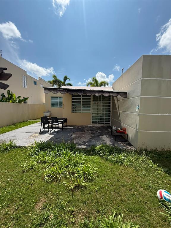 A backyard patio features a covered awning, metal security bars on windows, and a grassy lawn — Aurora 120 VEGA SERENA, VEGA BAJA, PR
