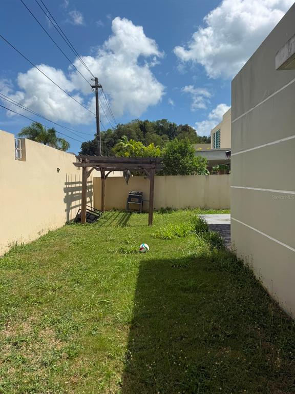 A grassy backyard features a wooden pergola, a small grill, and a perimeter wall — Aurora 120 VEGA SERENA, VEGA BAJA, PR