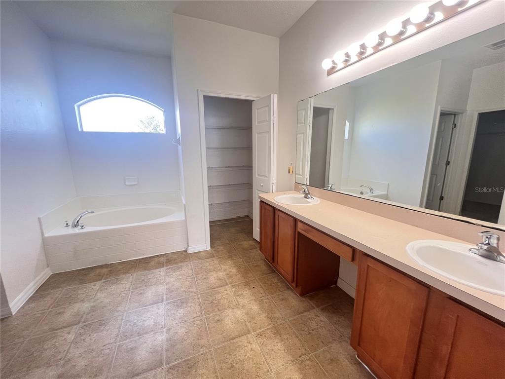 A bathroom features a soaking tub, a double vanity with wood cabinets, and a walk-in closet — 41 LOUISIANA DRIVE, PALM COAST, FL