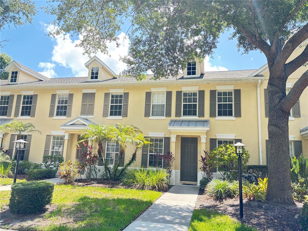 A two-story yellow townhouse with dark shutters and a front walkway under a large tree — 5641 WHITEHEAD STREET, BRADENTON, FL