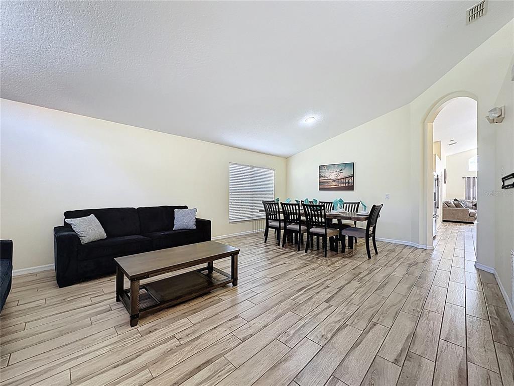 A living and dining area features light wood-look tile flooring and a black sofa — 110 RUBINO DRIVE, DAVENPORT, FL