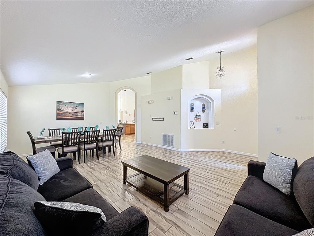 A living room with wood-look tile floors, dark sofas, and an adjacent dining area — 110 RUBINO DRIVE, DAVENPORT, FL