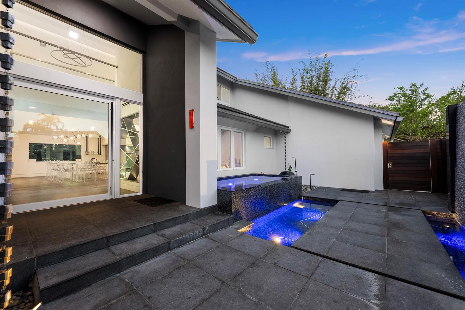 A modern home exterior features a tiered pool, dark stone patio, and large glass doors — 7047 San Sebastian Circle, Boca Raton FL 33433, BOCA RATON, FL