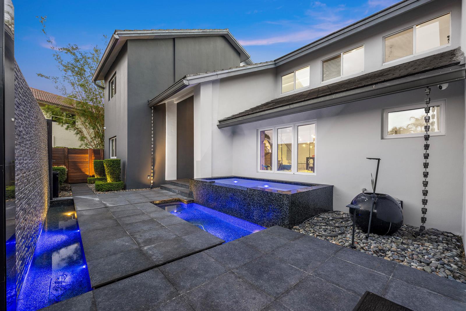 A modern home exterior features a tiled patio, a raised pool, and blue accent lighting — 7047 San Sebastian Circle, Boca Raton FL 33433, BOCA RATON, FL