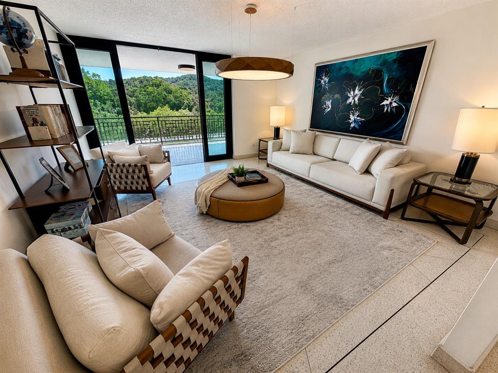 A modern living room features a large sofa, round ottoman, and balcony with forest views — B7 CALLE INDUSTRIA, CAGUAS, PR