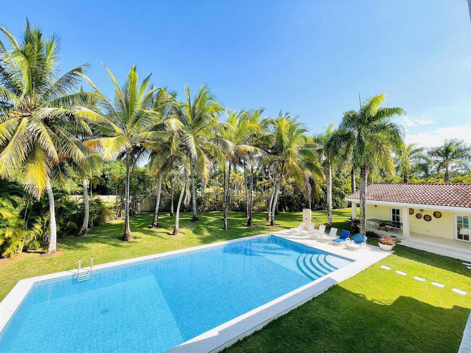 A rectangular swimming pool sits on a lawn beside a house with palm trees — 123 Sea Horse Ranch, FL