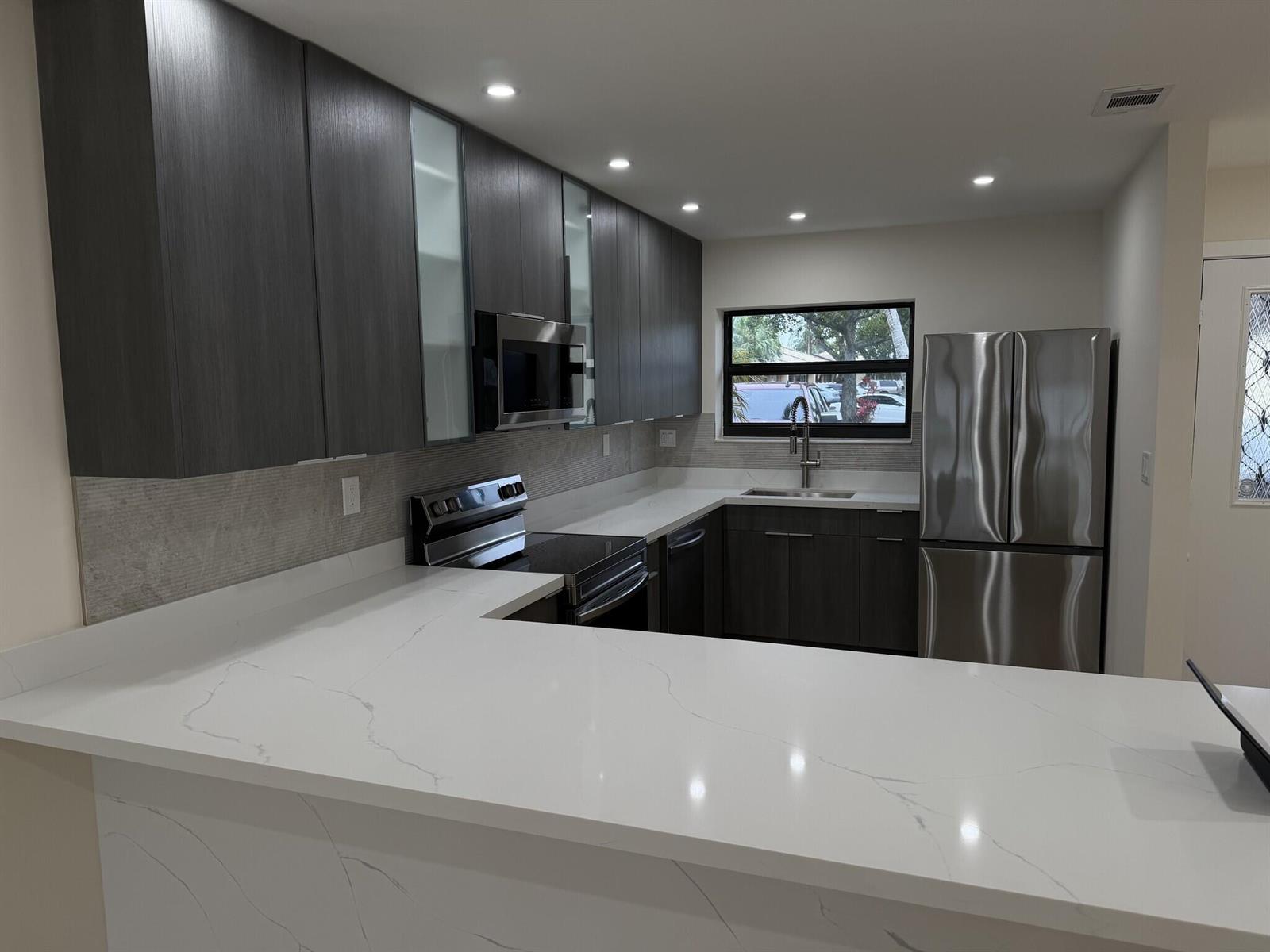 A modern kitchen features dark wood cabinets, white marble-look countertops, and stainless steel appliances — 705 Banks Road, Margate FL 33063, MARGATE, FL