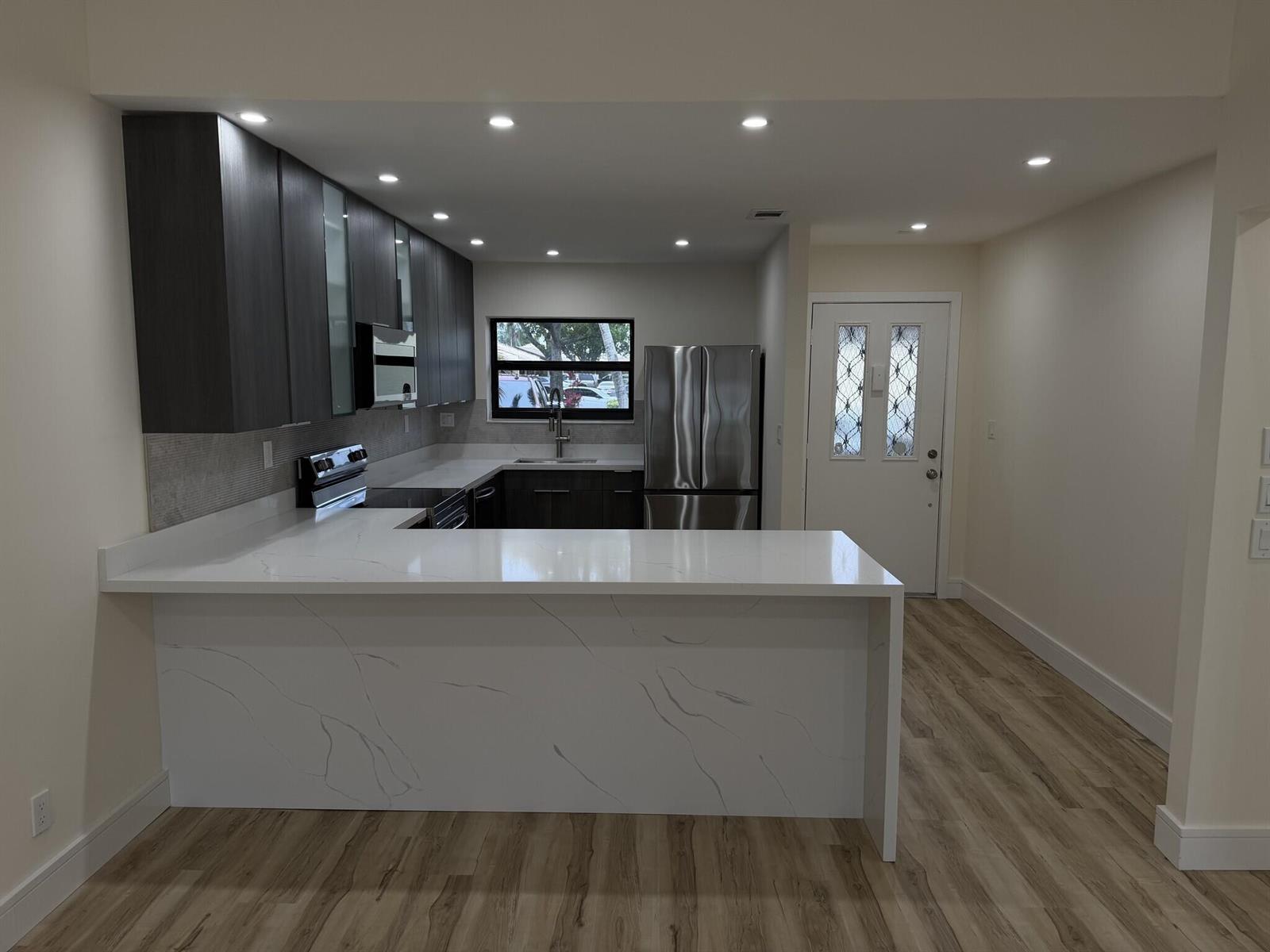 A modern kitchen features dark wood cabinets, white marble-style countertops, and stainless steel appliances — 705 Banks Road, Margate FL 33063, MARGATE, FL