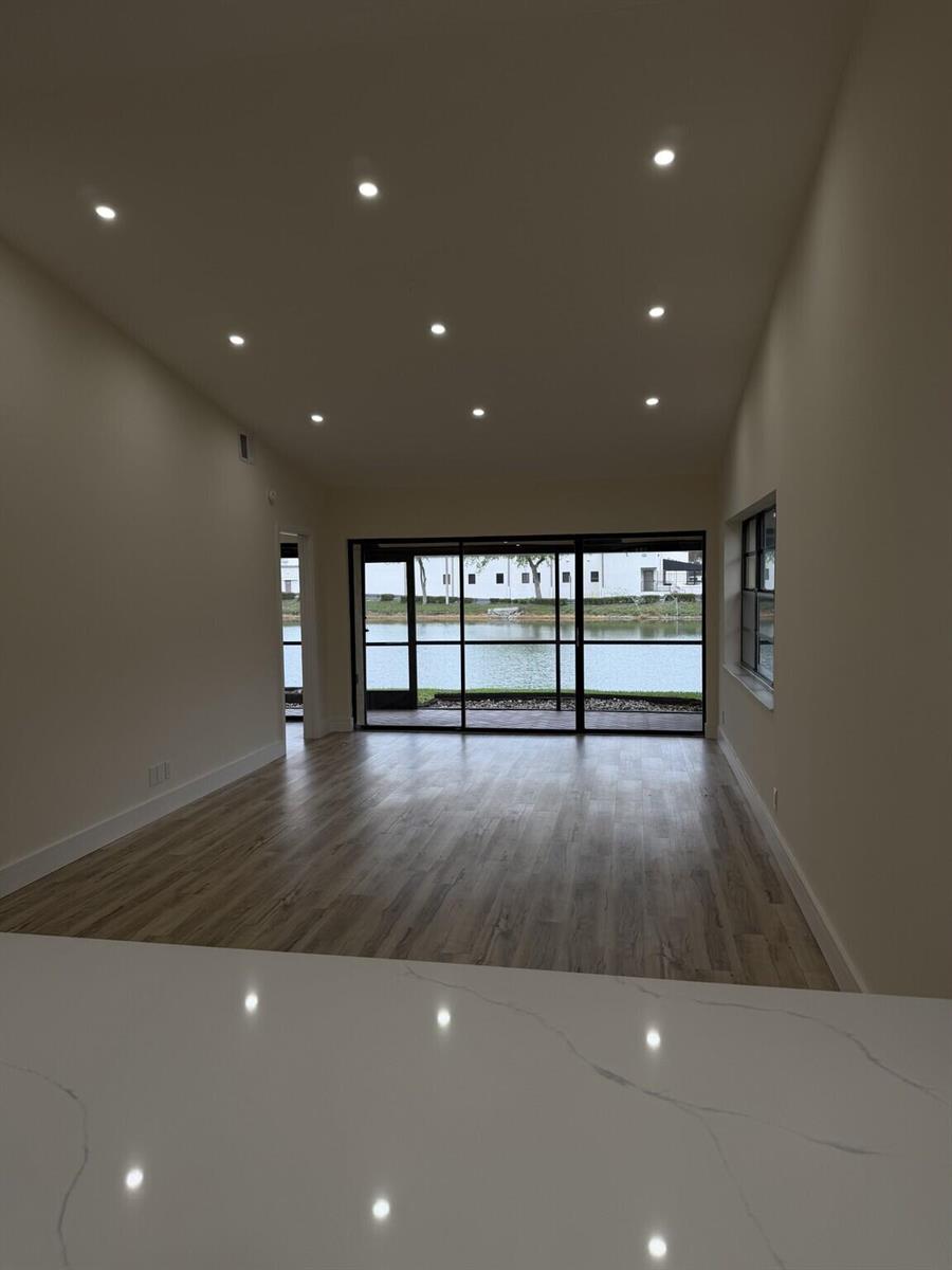 An empty room with wood-look flooring, recessed lighting, and large sliding doors overlooking a lake — 705 Banks Road, Margate FL 33063, MARGATE, FL