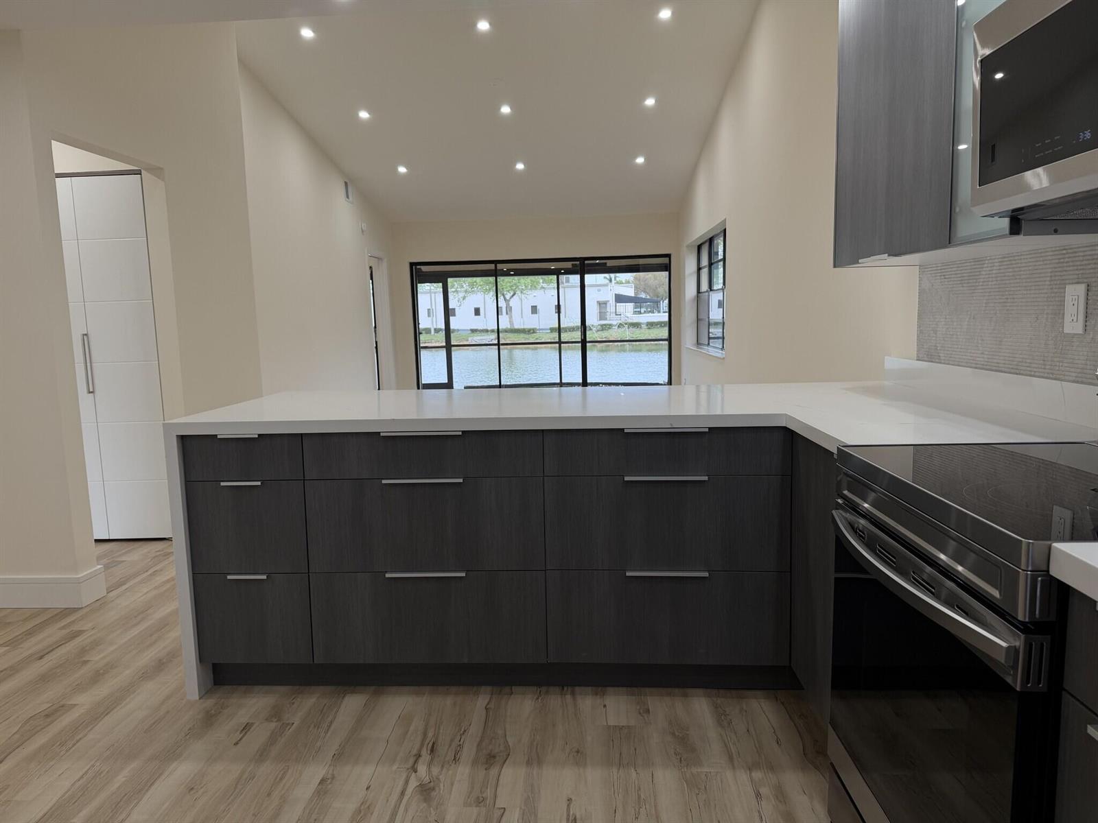 A modern kitchen features dark wood cabinetry, white countertops, and a view of a lake — 705 Banks Road, Margate FL 33063, MARGATE, FL