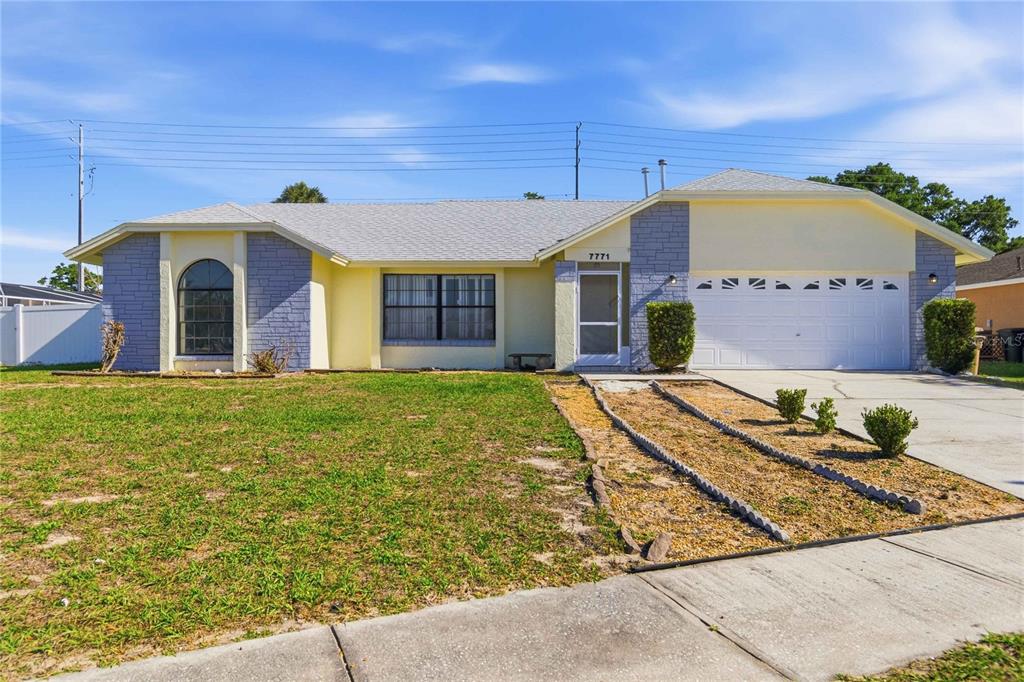 A single-story house with a light yellow exterior, blue stone accents, and a two-car garage — 7771 INDIAN RIDGE TRAIL N, KISSIMMEE, FL