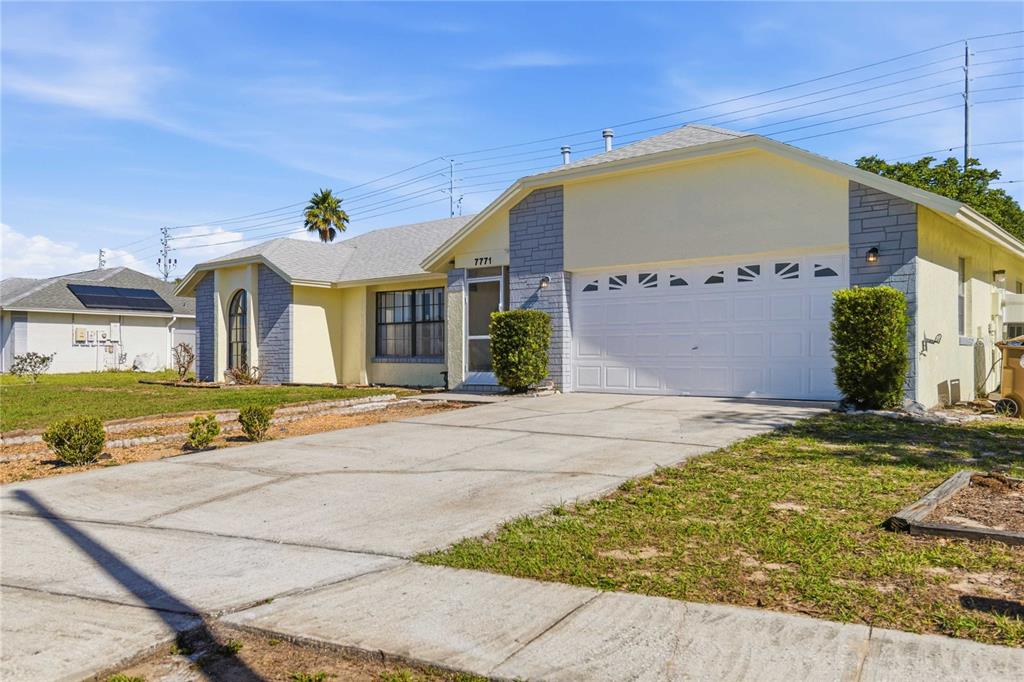 A single-story house with a yellow exterior, gray stone accents, and a white garage door — 7771 INDIAN RIDGE TRAIL N, KISSIMMEE, FL