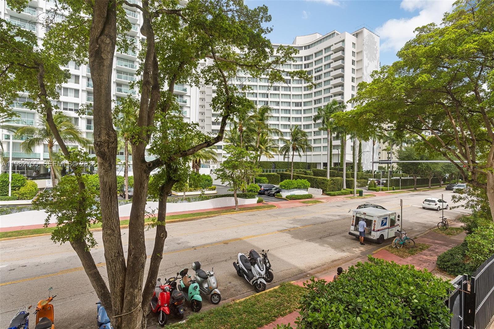 An exterior view of a large white apartment building with parked scooters and a mail truck — 1035 West Ave # 201, Miami Beach FL 33139, MIAMI BEACH, FL