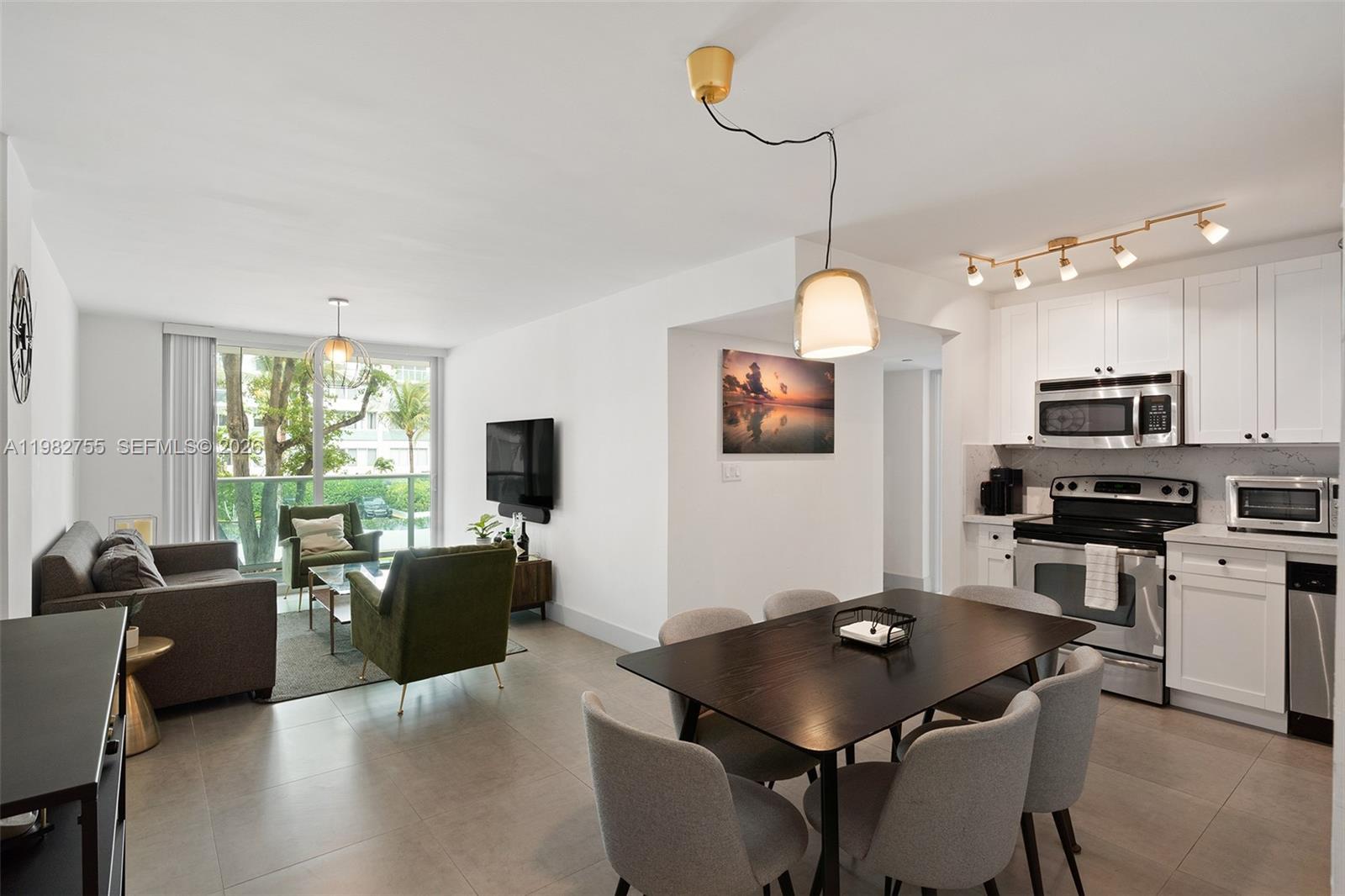 An open-concept living and dining area features white cabinets, stainless appliances, and tile flooring — 1035 West Ave # 201, Miami Beach FL 33139, MIAMI BEACH, FL