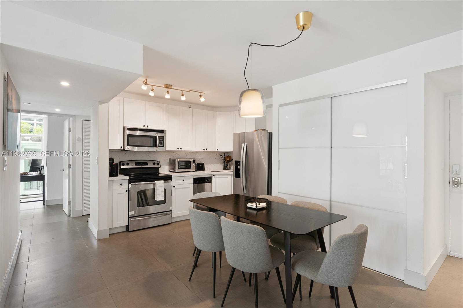 A modern kitchen features white cabinetry, stainless steel appliances, and a dark dining table — 1035 West Ave # 201, Miami Beach FL 33139, MIAMI BEACH, FL