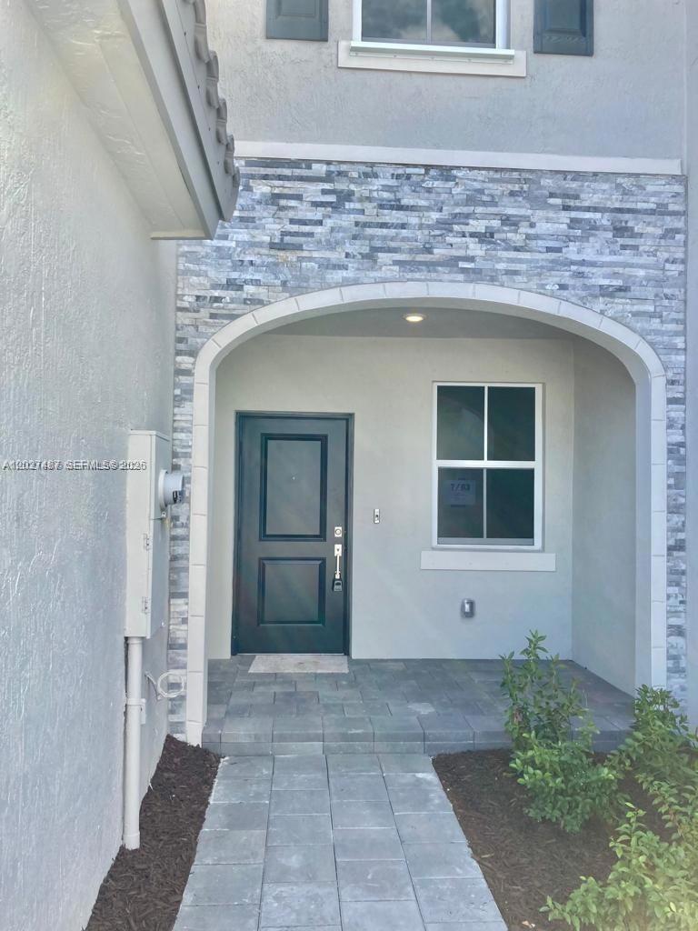 The exterior entrance features a dark door, stone veneer accents, and a paved walkway — 1070 SE 26th Ter, Homestead FL 33035, HOMESTEAD, FL