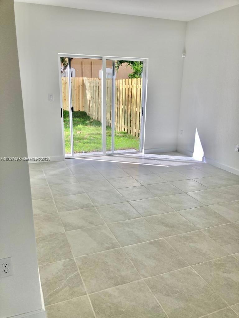 A room with light-colored tile flooring and a sliding glass door leading to a yard — 1070 SE 26th Ter, Homestead FL 33035, HOMESTEAD, FL