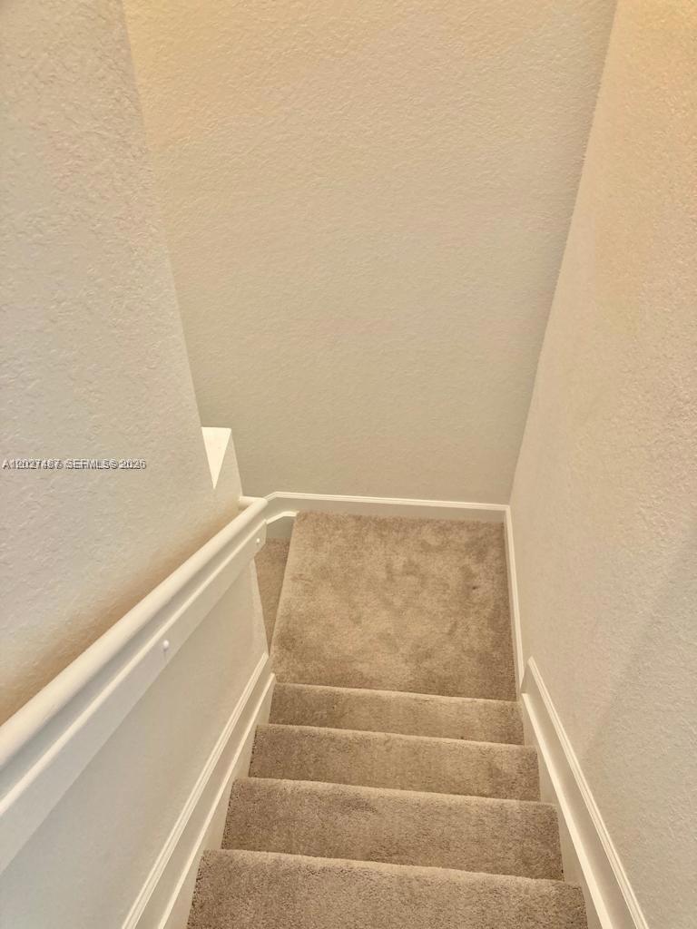 A carpeted staircase with a white handrail leads downward between two plain walls — 1070 SE 26th Ter, Homestead FL 33035, HOMESTEAD, FL
