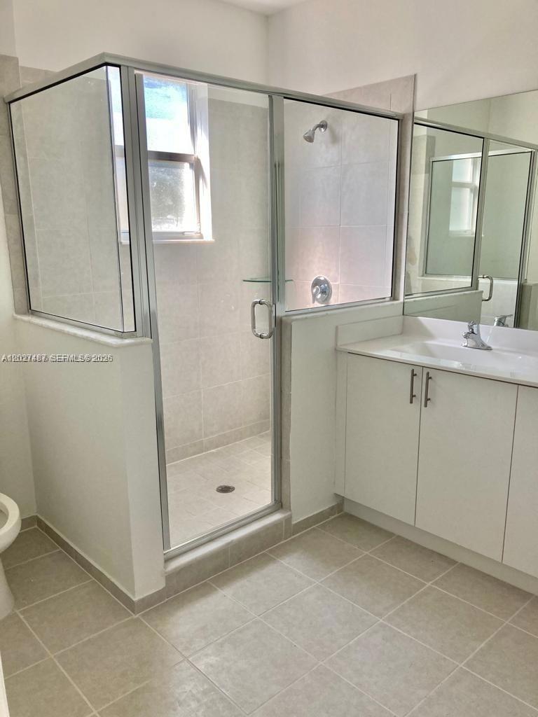 A bathroom features a glass-enclosed walk-in shower, a white vanity, and light-colored tile flooring — 1070 SE 26th Ter, Homestead FL 33035, HOMESTEAD, FL