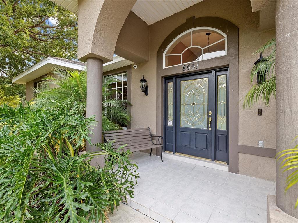 A covered entryway features a tiled porch, a dark front door, and a wooden bench — 8551 PRATT DRIVE, NEW PORT RICHEY, FL