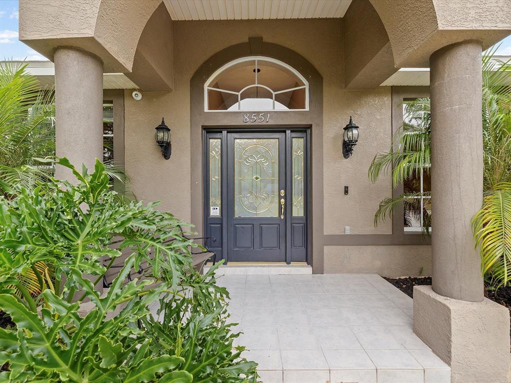 The front entrance features a dark gray door with glass panels under a covered porch — 8551 PRATT DRIVE, NEW PORT RICHEY, FL