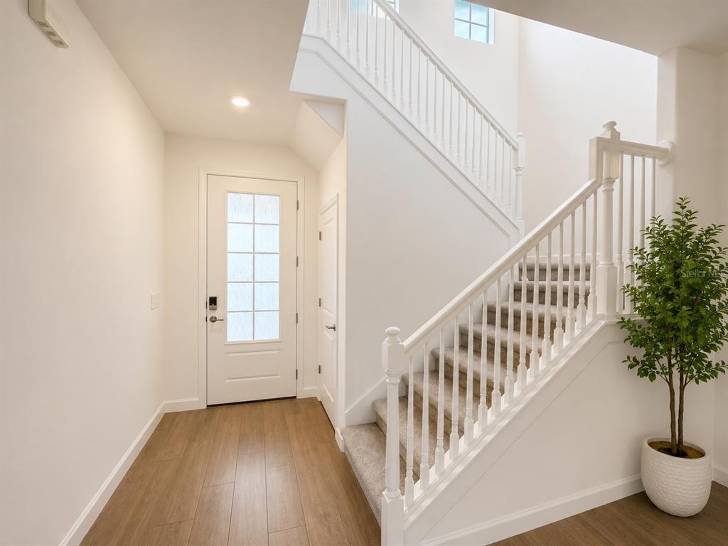 A bright entryway features wood-look flooring, a white front door, and a carpeted staircase — 15115 SEA SALT WAY, BRADENTON, FL