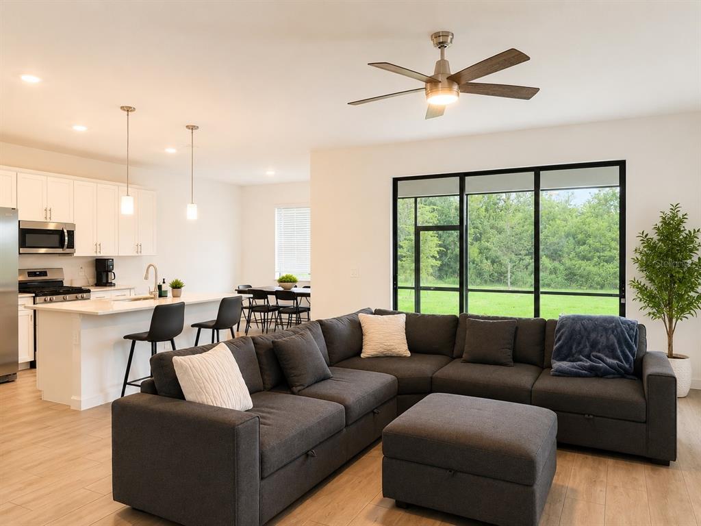 A modern open-concept living room and kitchen featuring a dark sectional sofa and large windows — 15115 SEA SALT WAY, BRADENTON, FL