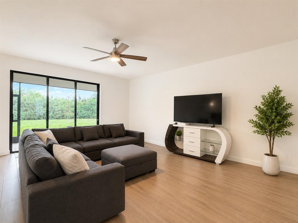 A living room features a dark sectional sofa, a modern white media console, and wood flooring — 15115 SEA SALT WAY, BRADENTON, FL