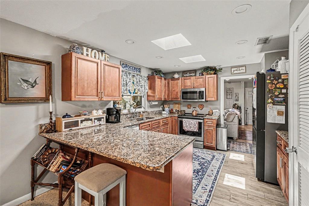 A kitchen features wood cabinets, granite countertops, a breakfast bar, and stainless steel appliances — 3100 SAUNDERS PLACE, TITUSVILLE, FL