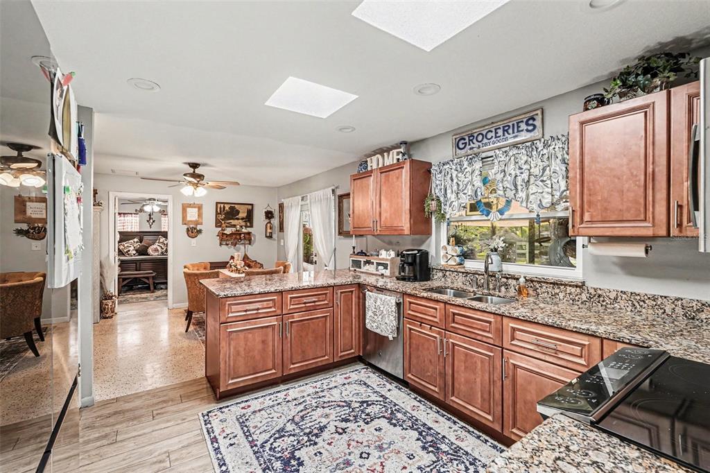A kitchen features wood cabinets, granite countertops, a patterned rug, and an adjacent dining area — 3100 SAUNDERS PLACE, TITUSVILLE, FL