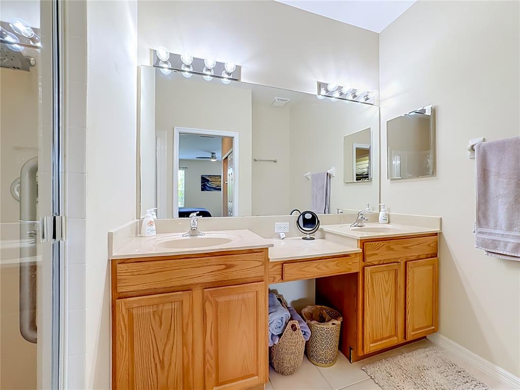 A bathroom features a double vanity with oak cabinets, a large mirror, and a shower — 4346 KARIBA LAKE TERRACE, SARASOTA, FL