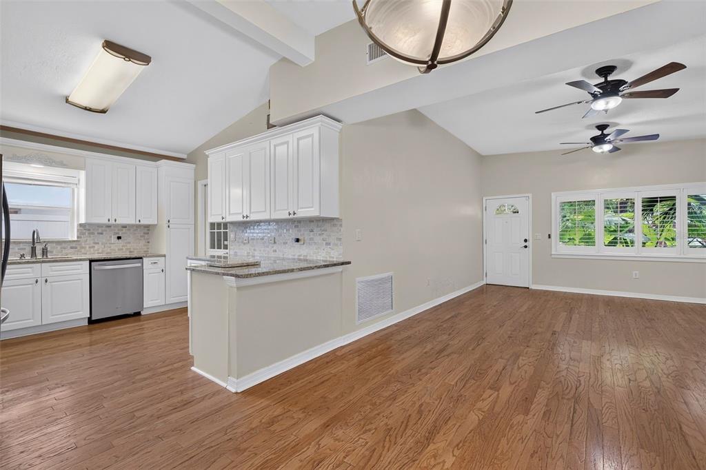 A kitchen with white cabinets and granite countertops opens into a living area with hardwood floors — 12496 136TH LANE, LARGO, FL