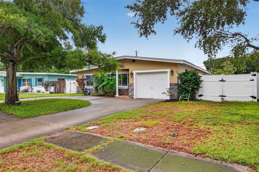 A single-story house with a tan exterior, stone accents, a white garage, and a white fence — 12496 136TH LANE, LARGO, FL