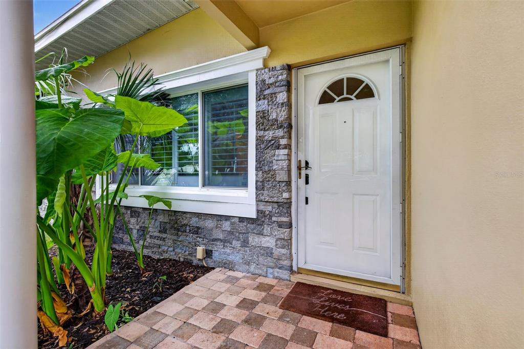A white front door with a decorative window sits next to a stone-accented wall — 12496 136TH LANE, LARGO, FL