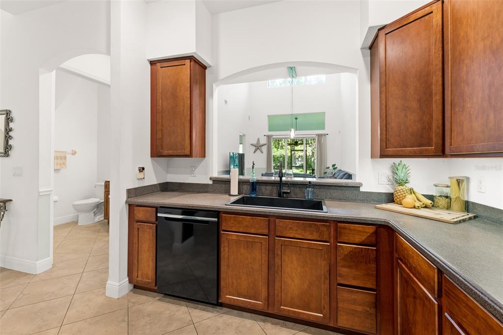 A kitchen features dark wood cabinets, a black dishwasher, and a sink overlooking a living area — 8414 MARIA COURT UNIT 5, CAPE CANAVERAL, FL