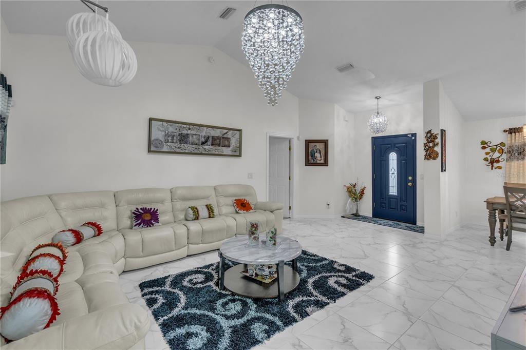 A living room with white tile floors, a white sectional sofa, and two crystal chandeliers — 5292 SW 115TH LOOP, OCALA, FL
