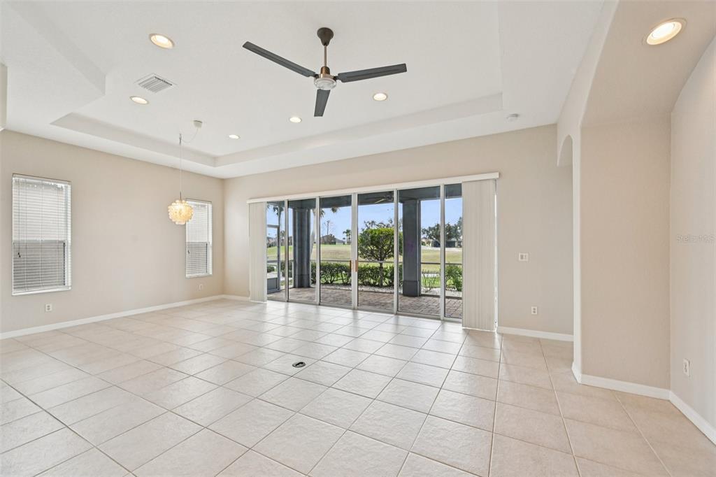 A spacious, tiled living room features a tray ceiling, ceiling fan, and large sliding glass doors — 819 REGAL MANOR WAY, SUN CITY CENTER, FL