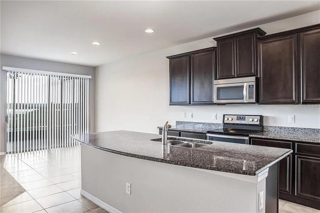 A kitchen features dark wood cabinets, granite countertops, a center island, and stainless steel appliances — 9215 MOUNTAIN MAGNOLIA DRIVE, RIVERVIEW, FL