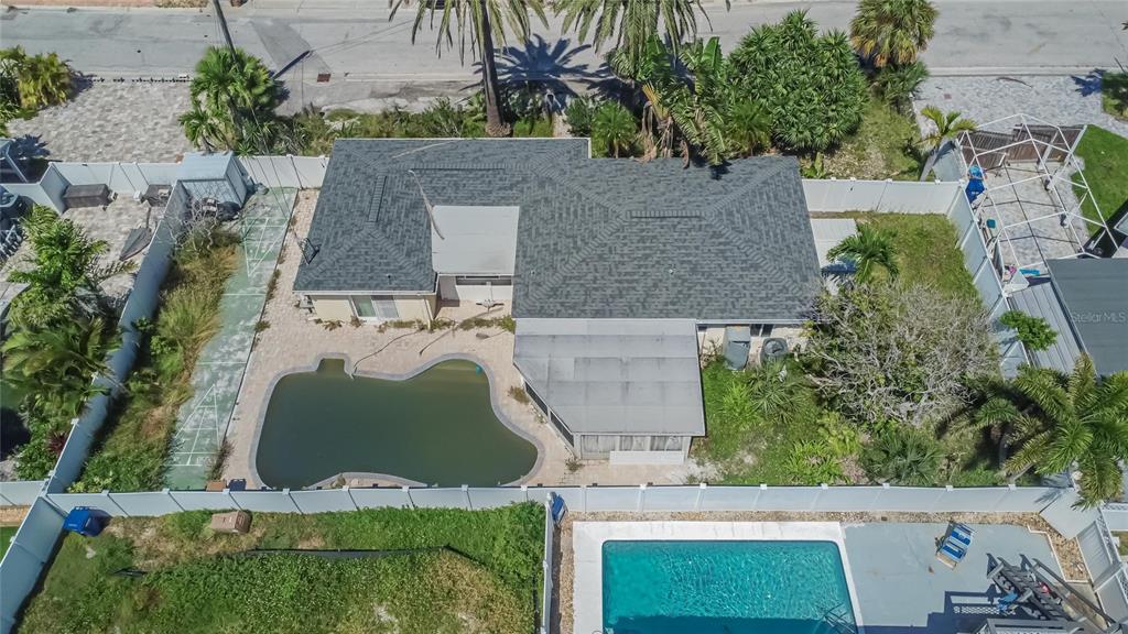 An aerial view shows a house with a dark roof, a pool, and a fenced yard — 363 145TH AVENUE E, MADEIRA BEACH, FL