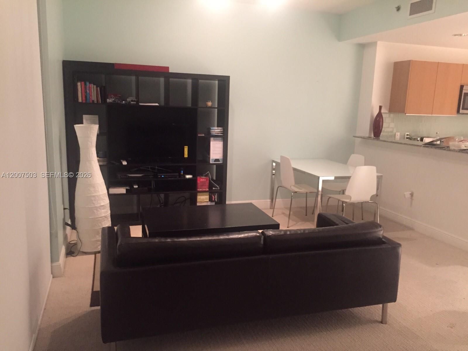 A living room features a black sofa, a media shelving unit, and a small dining area — 1050 Brickell Ave # 2312, Miami FL 33131, MIAMI, FL