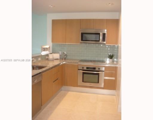 A kitchen features light wood cabinets, stainless steel appliances, and a light green subway tile backsplash — 1050 Brickell Ave # 2312, Miami FL 33131, MIAMI, FL