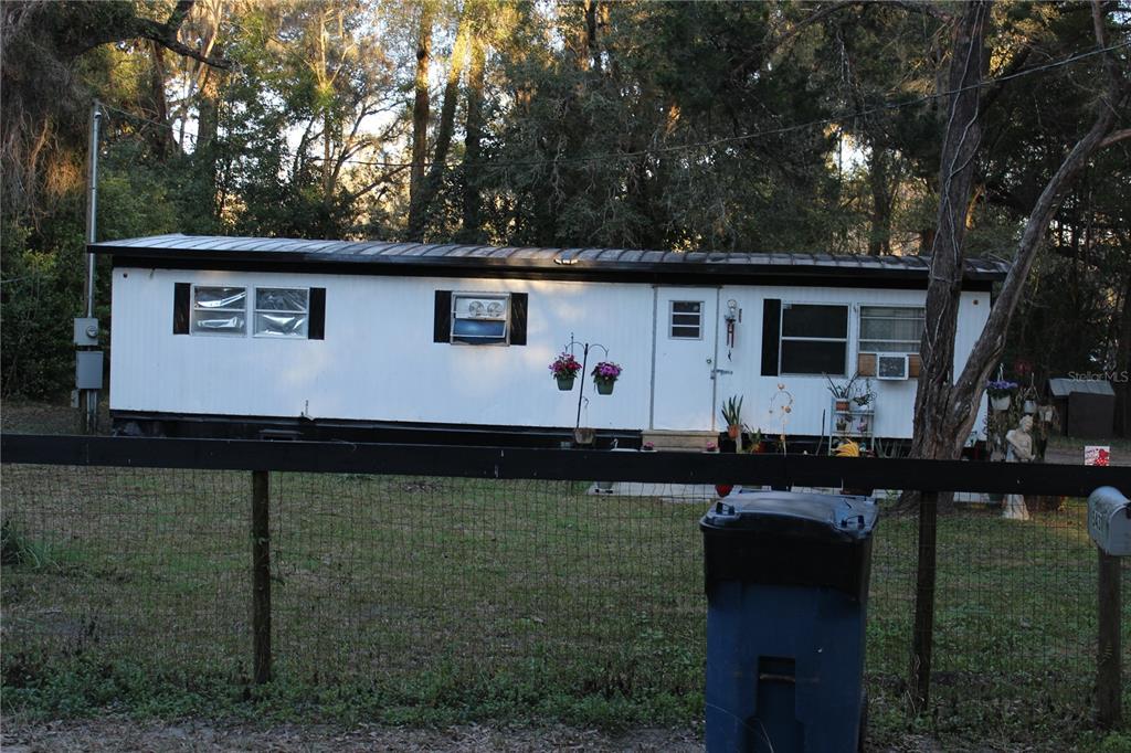 A single-wide mobile home with white siding sits behind a wire fence and trees — 5380 SE 28TH COURT, OCALA, FL