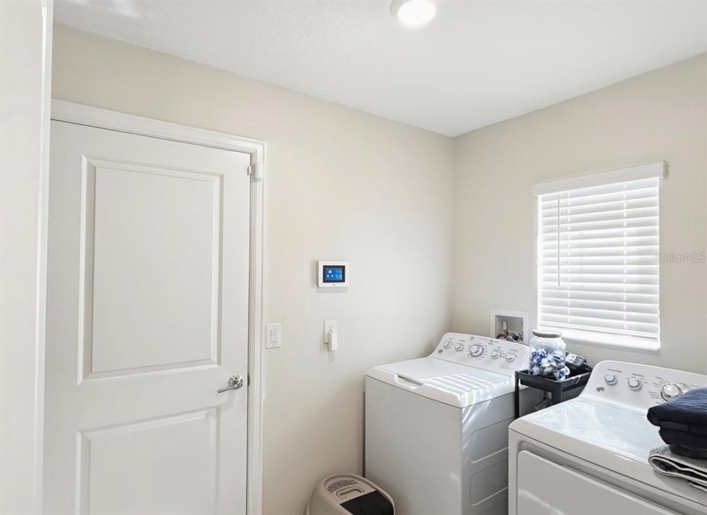 A laundry room features white appliances, a window with blinds, and a wall-mounted control panel — 1988 TRAVERSE WAY, KISSIMMEE, FL
