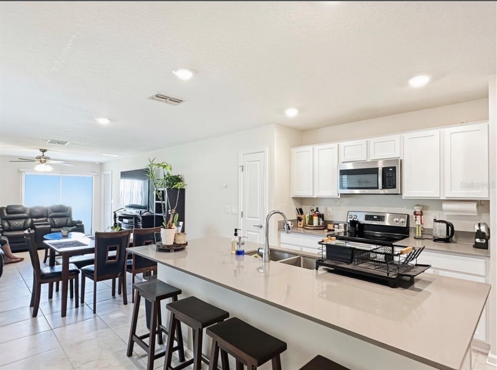 A kitchen with white cabinets and a large island overlooks an open-concept dining and living area — 1988 TRAVERSE WAY, KISSIMMEE, FL