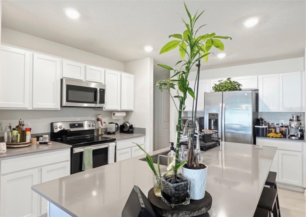 A kitchen features white cabinets, stainless steel appliances, and a large central island with seating — 1988 TRAVERSE WAY, KISSIMMEE, FL